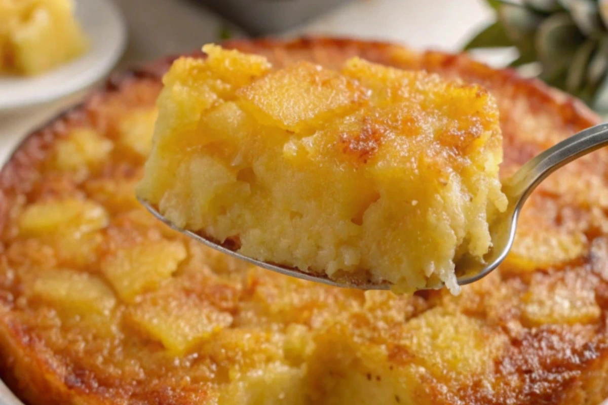 A spoon lifting a serving of pineapple upside-down cake, showing the soft, moist texture with chunks of pineapple on top.